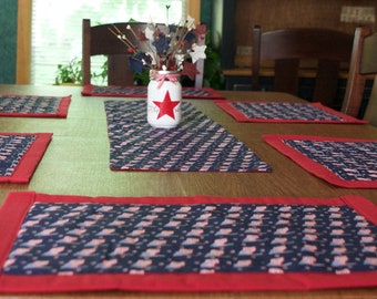 Peut inclure: Une table à manger en bois avec des sets de table rouge et bleu. Les sets de table ont un motif d'étoiles et de rayures. Un bocal en verre transparent avec une étoile rouge est au centre de la table.