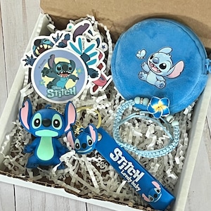 May include: A gift box filled with Stitch-themed merchandise. Includes stickers, a blue coin purse, a bracelet, a keychain, and a figurine. The items are blue and white, with the word "Stitch" on some items.