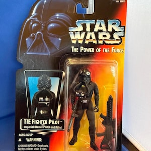 May include: A Star Wars action figure of a TIE Fighter Pilot, packaged on a card with the Star Wars logo and "The Power of the Force" text. The figure is black and comes with a blaster pistol and rifle. Ages 4 & up.