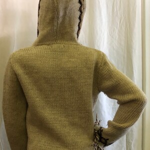May include: A beige knitted hooded sweater with brown and black geometric patterns on the hood and sleeves.
