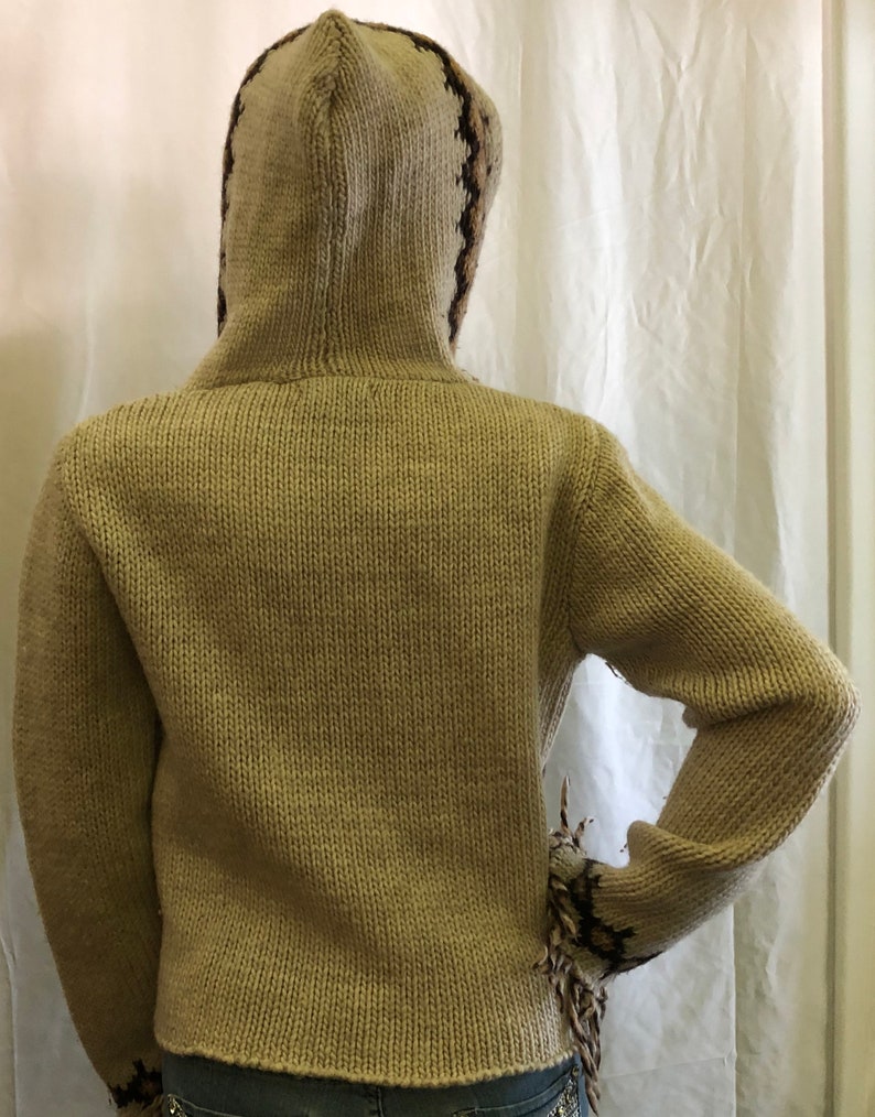 May include: A beige knitted hooded sweater with brown and black geometric patterns on the hood and sleeves.