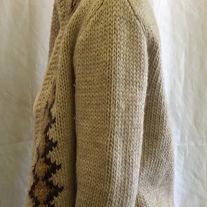 May include: A cream-colored knitted cardigan with brown and tan geometric patterns on the sleeves and hood. The cardigan has a fringed hem and is made of a soft, cozy material.