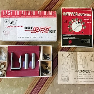May include: A vintage sewing kit with "Dot Snappers Kit" and "Gripper Fasteners" packaging. The kit includes a box with tools and instructions, and a red and white box with snap fasteners. The text reads "Easy to attach at home."