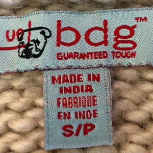 May include: A blue and white woven label with the text "bdg" in red and "Guaranteed Tough" in black. A smaller blue and white label below reads "Made in India Fabrique en Inde S/P".