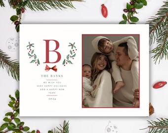Op de afbeelding: Een kerstkaart met een rode en groene krans met een grote rode letter "B" in het midden. De krans is versierd met hulstbladeren en rode bessen. De kaart bevat ook een foto van een gezin van vier, met een rode strik bovenaan. De tekst op de kaart luidt "The Banks, We wish you very happy holidays and a happy new year! 2024."