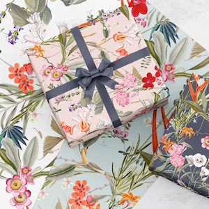 May include: Three gift boxes wrapped in floral patterned paper. The top box is pink with a gray ribbon, the middle box is blue with a white floral pattern, and the bottom box is dark blue with a white floral pattern.
