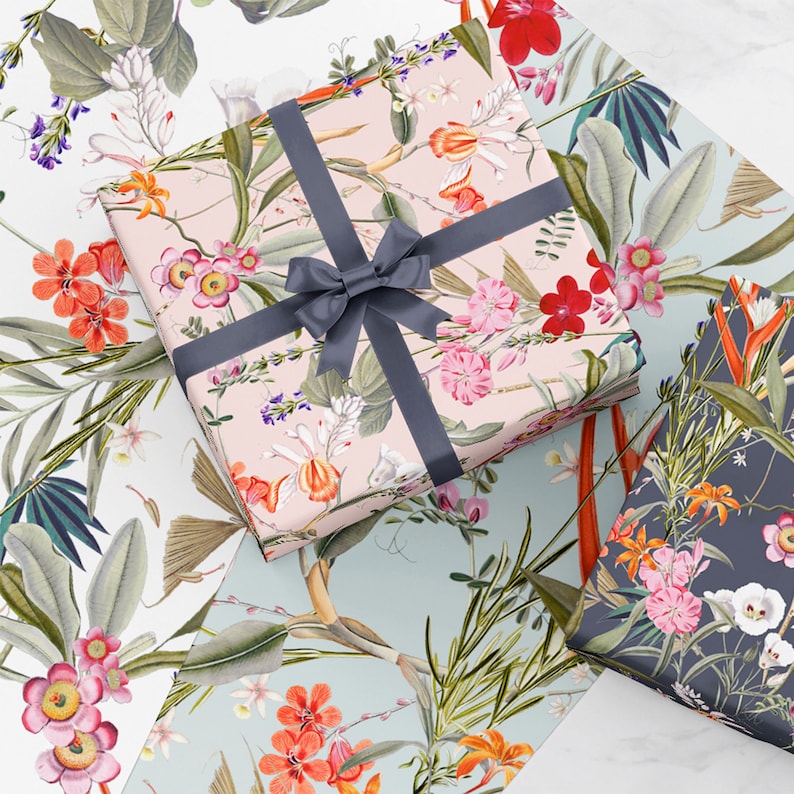 May include: Three gift boxes wrapped in floral patterned paper. The top box is pink with a gray ribbon, the middle box is blue with a white floral pattern, and the bottom box is dark blue with a white floral pattern.