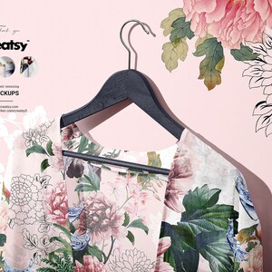 May include: A floral print kimono hanging on a black wooden hanger against a pink background. The kimono has a white background with pink, blue, and green floral patterns.
