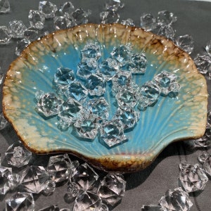 May include: A blue and brown ceramic shell-shaped dish filled with clear crystal-like beads. The beads are faceted and have a diamond-like shape.