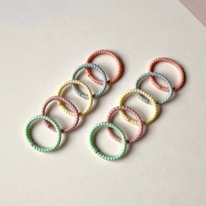 Puede incluir: Un conjunto de ocho gomas para el pelo de colores en tonos pastel de rosa, azul, amarillo y verde. Las gomas para el pelo est&aacute;n hechas de un material suave y el&aacute;stico y son perfectas para sujetar el pelo.
