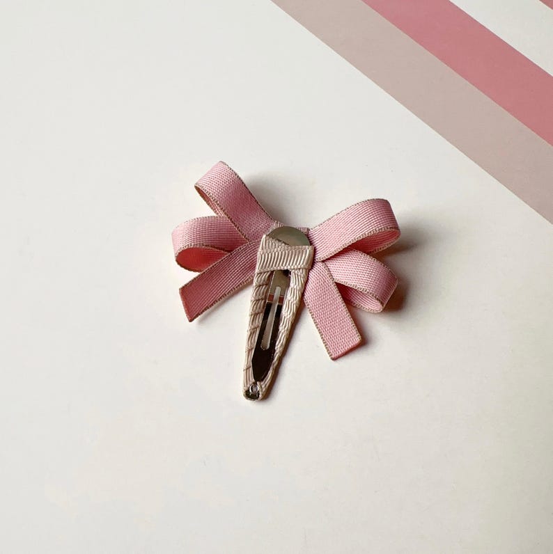 May include: A pink satin bow hair clip with a silver clip.