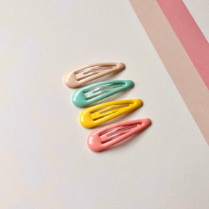 Może przedstawiać: Cztery plastikowe spinki do włos&oacute;w w pastelowych kolorach. Spinki są w odcieniach r&oacute;żowego, ż&oacute;łtego, niebieskiego i brzoskwiniowego.