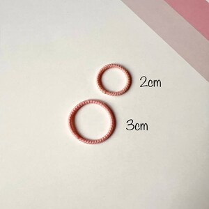 Puede incluir: Dos gomas para el pelo de color rosa, una con un di&aacute;metro de 2 cm y la otra con un di&aacute;metro de 3 cm.