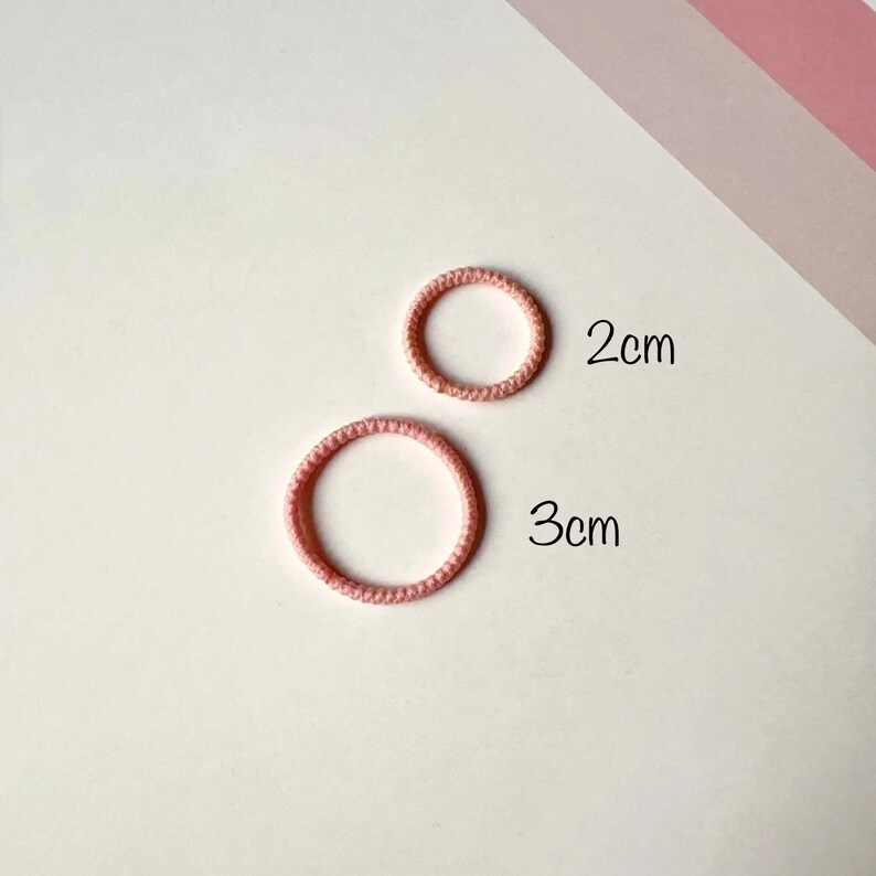 Puede incluir: Dos gomas para el pelo de color rosa, una con un di&aacute;metro de 2 cm y la otra con un di&aacute;metro de 3 cm.