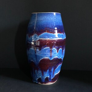 May include: A blue and purple ceramic vase with a wavy, abstract design. The vase is glazed and has a glossy finish.