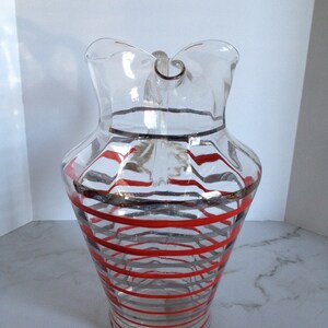 May include: A clear glass pitcher with a red and gray striped design. The pitcher has a wide mouth and a handle.