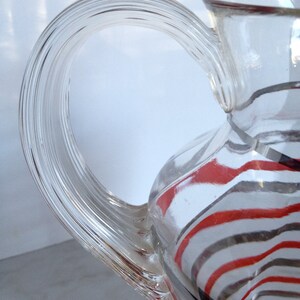 May include: A clear glass pitcher with a twisted handle. The pitcher has red and black stripes.