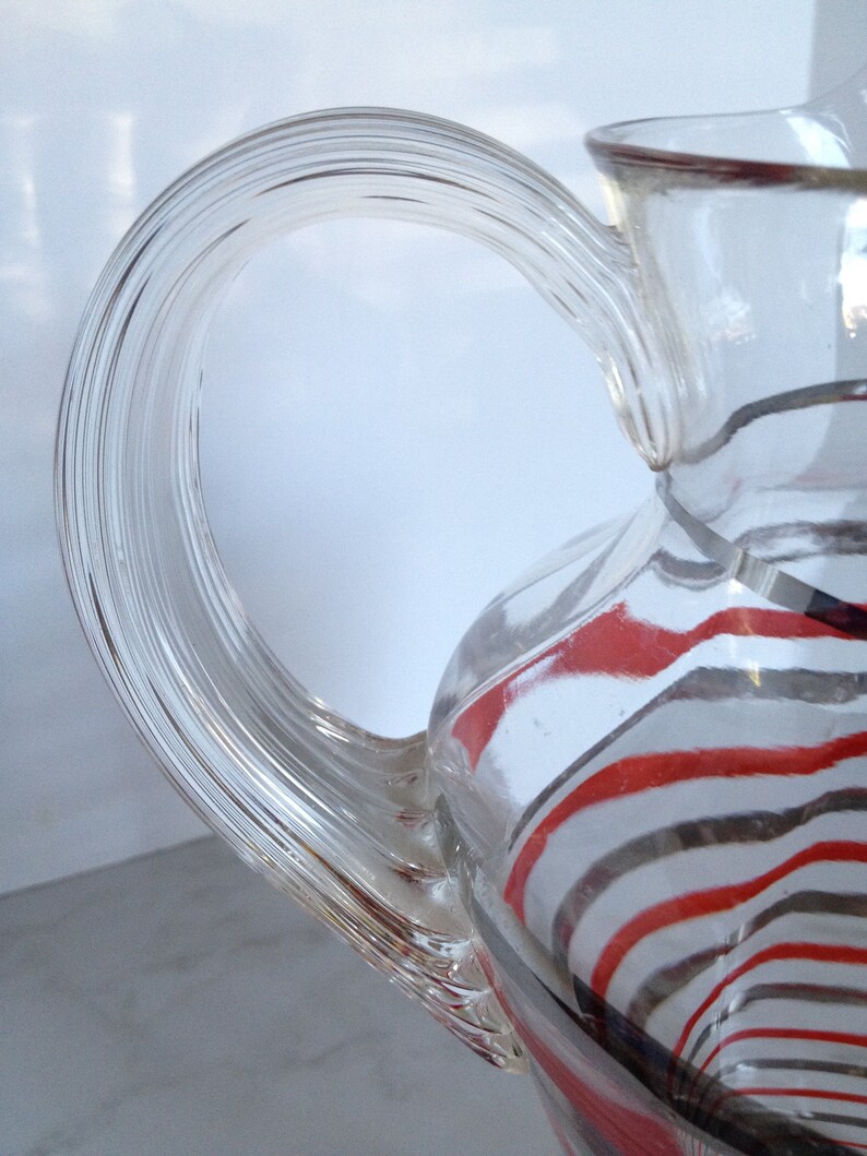 May include: A clear glass pitcher with a twisted handle. The pitcher has red and black stripes.