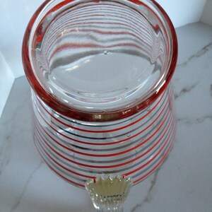 May include: A clear glass pitcher with a red and gray striped pattern. The pitcher has a handle with a decorative design.