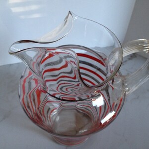 May include: A clear glass pitcher with a red and gray striped design. The pitcher has a wide mouth and a curved handle.
