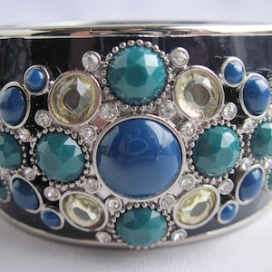 May include: A black bangle bracelet with a silver-toned metal design featuring a cluster of blue, green, and clear rhinestones.