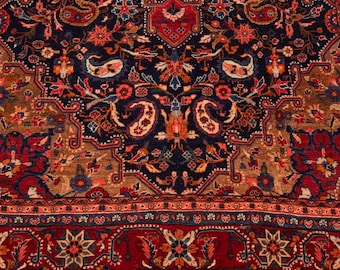 May include: A rectangular area rug featuring a dark navy blue center field with intricate floral and paisley motifs in shades of red, orange, and tan. The wide border displays a repeating pattern of star-like flowers on a deep red background.
