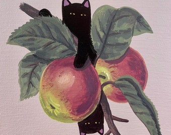May include: A painting of two red apples with green leaves on a branch. Two black cats are hanging from the branch, peeking out from behind the apples.