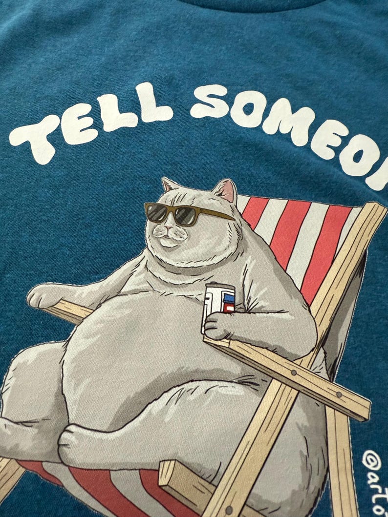 May include: Teal t-shirt featuring a cartoon cat wearing sunglasses, relaxing in a beach chair, and holding a beverage. The text "TELL SOMEONE" is arched across the top in white letters. The cat is gray, and the chair has red and white stripes.