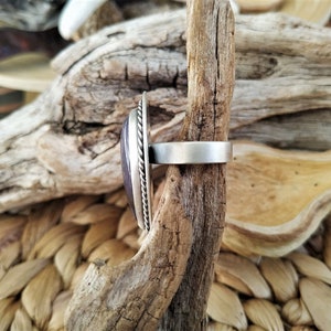 May include: A silver ring with a large, oval, purple stone. The stone is set in a silver bezel with a twisted rope design around the edge. The ring band is a simple, brushed silver.