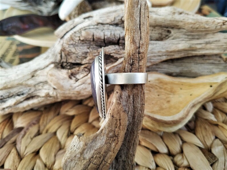 May include: A silver ring with a large, oval, purple stone. The stone is set in a silver bezel with a twisted rope design around the edge. The ring band is a simple, brushed silver.