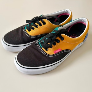 May include: Pair of black, yellow, and teal canvas sneakers with black laces. The shoes have a white sole and a pink logo tag. The interior is pink and black.