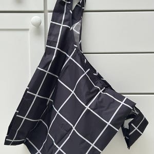 May include: A black and white checkered reusable shopping bag. The bag is folded and hanging from a hook.