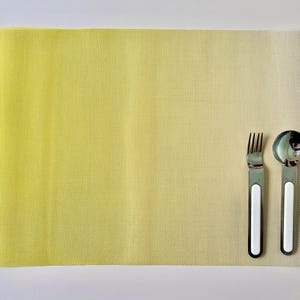 May include: A yellow and white gradient placemat with a fork and spoon on top. The fork and spoon have white handles.