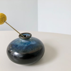 May include: A small, round, blue and black ceramic vase with a single yellow flower.