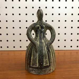 May include: A ceramic figurine of a woman in a black and green dress. The figurine is standing with her arms crossed in front of her.