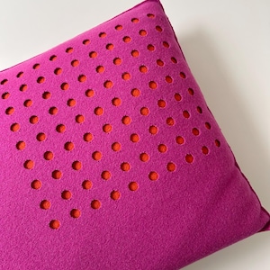 Peut inclure: Un coussin rectangulaire magenta avec un motif de cercles orange. Les cercles sont espacés uniformément sur la surface. Le coussin a un aspect doux et texturé.