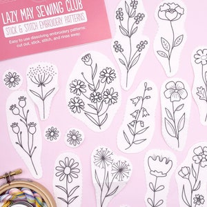 May include: A set of 13 white paper embroidery patterns featuring various flower designs. The patterns are cut out and ready to be used for embroidery projects. The text on the card reads "Lazy May Sewing Club Stick & Stitch Embroidery Patterns Easy to use dissolving embroidery patterns: cut out, stick, stitch, and rinse away."