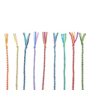 A neat row of finished friendship bracelets, each one woven in a different colour combination using the rainbow threads. The kit makes plenty to keep and share with friends.