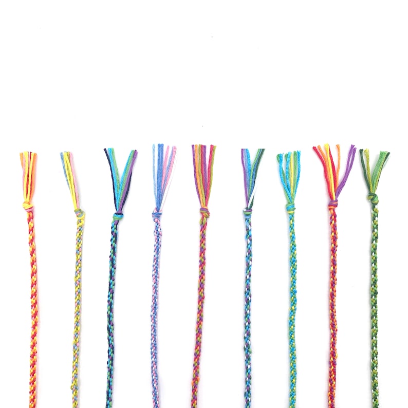 A neat row of finished friendship bracelets, each one woven in a different colour combination using the rainbow threads. The kit makes plenty to keep and share with friends.