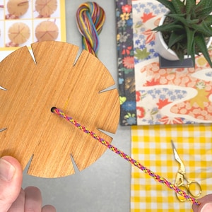 The bracelet loom in action, with threads being woven into a braid. This part of the process is simple and calming — ideal for beginners and a lovely activity for rainy afternoons or craft night fun.