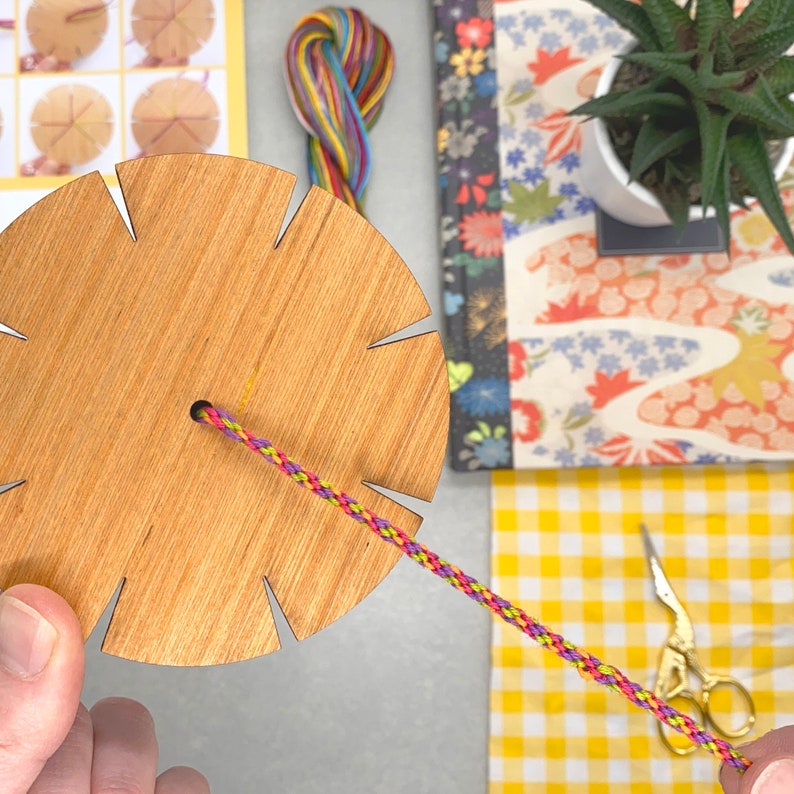 The bracelet loom in action, with threads being woven into a braid. This part of the process is simple and calming — ideal for beginners and a lovely activity for rainy afternoons or craft night fun.