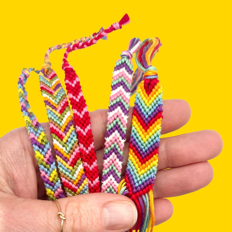 A hand holding multiple handmade friendship bracelets in bright colours. Perfect for beginners, this DIY bracelet making kit includes embroidery thread and instructions.