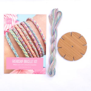 May include: Friendship bracelet kit with pastel colored embroidery floss, a wooden loom, and instructions on how to weave your own colorful bracelets. The kit includes the text "Friendship Bracelet Kit" and "Weave your own colorful bracelets".