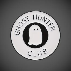 May include: White enamel pin with a black outline. The pin features a ghost with two eyes and the text "Ghost Hunter Club".