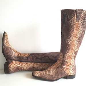 Puede incluir: Un par de botas altas de piel de serpiente marrón y beige con punta.