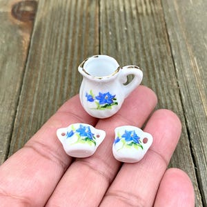 May include: A miniature tea set featuring a white teapot and two cups. The teapot and cups are decorated with blue flowers and gold trim.