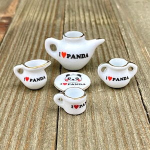 May include: A miniature white porcelain tea set with gold trim, featuring the text "I ❤️ PANDA" and a panda illustration. The set includes a teapot, creamer, sugar bowl, and a small cup and saucer.