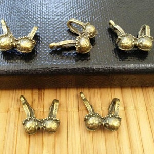 May include: Six gold-toned metal charms shaped like brassieres. The charms are small and detailed, with a delicate design.