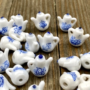 Puede incluir: Una colección de teteras de porcelana en miniatura con diseños florales azules y blancos. Las teteras son de diferentes formas y tamaños, y están dispuestas en un patrón aleatorio sobre una superficie de madera.