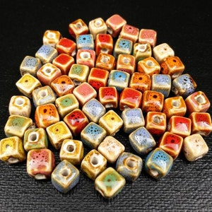 May include: A collection of colorful ceramic square beads with a hole in the center. The beads are speckled with various colors, including blue, green, yellow, orange, red, and brown.